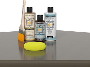 Retique It® Black Walnut kit with brush, Wood’n Primer, gloss top coat, and yellow sponge on a wood surface.