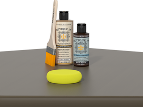 Retique It® Black Walnut Kit with Light Wood’n Primer, Black Walnut Gel Stain Alternative, paintbrush, and yellow sponge on a dark wood tabletop.