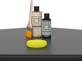Retique It® Classic Black Kit with Light Wood’n Primer, Classic Black Gel Stain Alternative, paintbrush, and yellow sponge on a black tabletop.