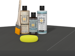 Retique It® Light Wood Wood’n Primer with Charcoal Gel Stain Alternative, matte topcoat, brush, and yellow sponge on a dark tabletop.