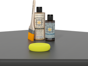 Retique It® Charcoal Kit with Light Wood’n Primer, Charcoal Gel Stain Alternative, paintbrush, and yellow sponge on a charcoal gray tabletop.