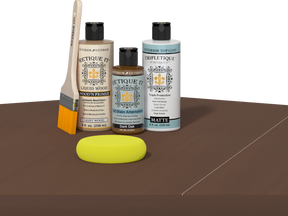 Retique It® Light Wood Wood’n Primer with Dark Oak Gel Stain Alternative, matte topcoat, brush, and yellow sponge on a tabletop.