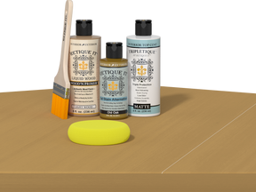 Retique It® Light Wood Wood’n Primer with Old Oak Gel Stain Alternative, matte topcoat, brush, and yellow sponge on a tabletop.