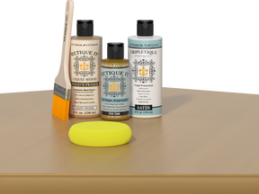 Retique It® Light Wood Wood’n Primer with Old Oak Gel Stain Alternative, satin topcoat, brush, and yellow sponge on a tabletop.