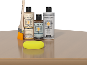 Retique It® Pecan Multipurpose Kit contents with Light Wood Liquid Wood primer, Pecan gel stain alternative, PolyTique It® gloss exterior top coat, paintbrush, and yellow sponge displayed on a wood surface.