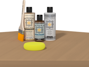 Retique It® Pecan Multipurpose Kit contents with Light Wood Liquid Wood primer, Pecan gel stain alternative, PolyTique It® matte exterior top coat, paintbrush, and yellow sponge displayed on a wood surface.
