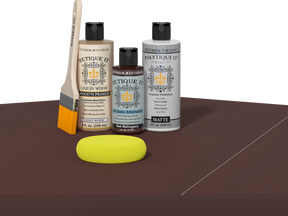Retique It® Light Wood Wood’n Primer with Red Mahogany Gel Stain Alternative, matte topcoat, brush, and yellow sponge on a dark tabletop.