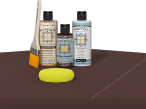 Retique It® Light Wood Wood’n Primer with Red Mahogany Gel Stain Alternative, matte topcoat, brush, and yellow sponge on a dark tabletop.