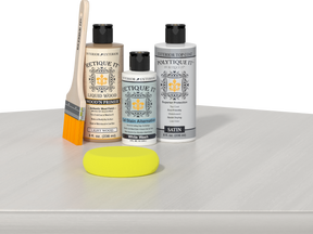Retique It® Light Wood Wood’n Primer with White Wash Gel Stain Alternative, satin topcoat, brush, and yellow sponge on a white tabletop.