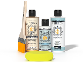 Retique It® Light Wood Wood’n Primer with White Wash Gel Stain Alternative, matte topcoat, brush, and yellow sponge on a reflective tabletop.