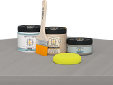 Retique It® Weathered Wood Multipurpose Kit contents with Light Wood Liquid Wood primer, Weathered Wood gel stain alternative, Tripletique matte interior top coat, paintbrush, and yellow sponge displayed on a gray wood surface.