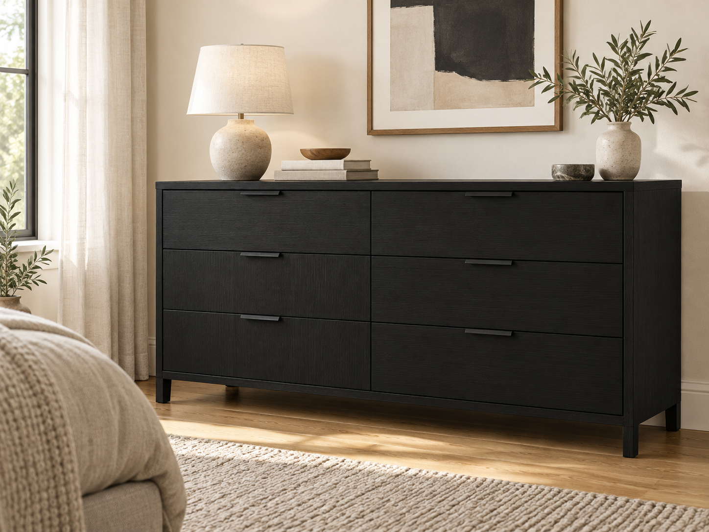Ebony six-drawer dresser topped with a lamp, books, and greenery in a neutral bedroom.