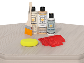 Set of wood care products including bottles, a brush, and sponges on a textured surface.