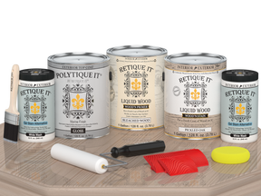 Sun-bleached Retique It® Wood'n Finish Kit for exterior wood, with four large top coat bottles displayed on a table.