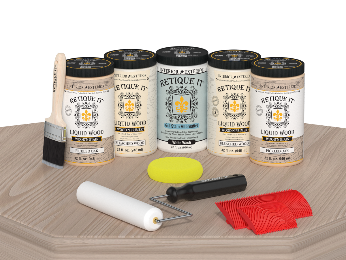 Retique It® Sun Bleached finishing system displayed on a light wood surface, featuring Liquid Wood Wood’n Primer in Bleached Wood, Liquid Wood Wood’n Stain in Pickled Oak, White Wash Gel Stain Alternative, paintbrush, roller, yellow sponge, and red graining tools for creating a weathered sun-bleached wood finish.