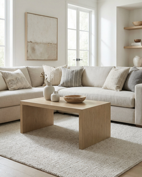 Bright neutral living room with a cream sectional sofa, light wood coffee table, and textured rug.
