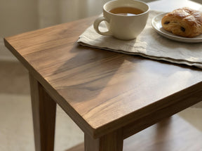 Close-up of a dark stained wood tabletop with a cup of tea and pastry in warm sunlight.