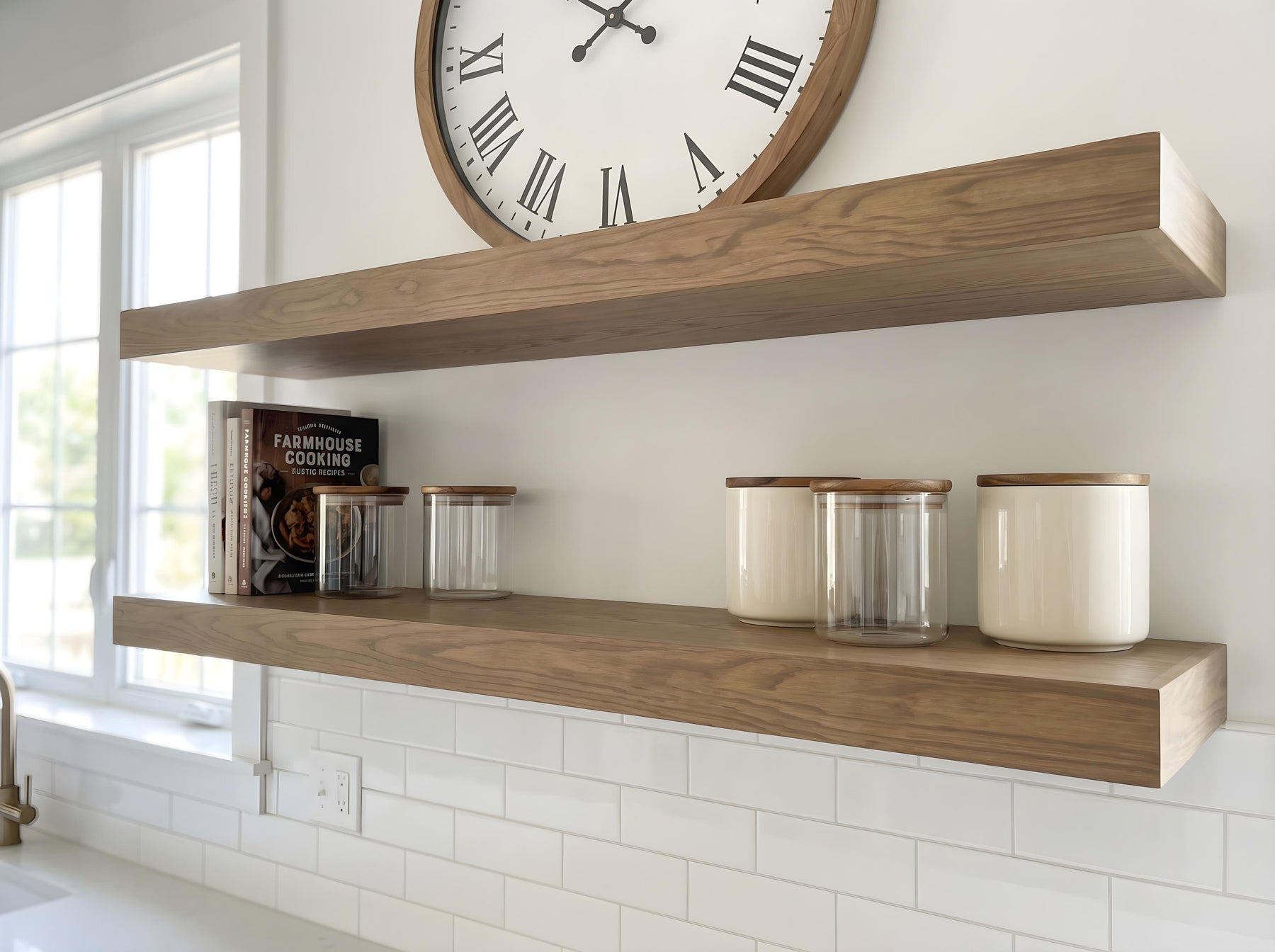Two floating wooden kitchen shelves mounted on a white wall above a white subway tile backsplash. The top shelf is styled with a large round clock, and the lower shelf holds a cookbook and several glass canisters with wooden lids.