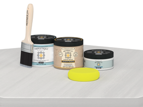 Painting supplies including a brush, containers of paint, and a sponge on a white surface.