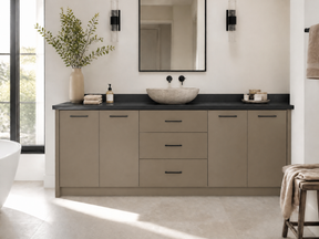A modern bathroom vanity featuring a matte taupe-gray cabinet with a black countertop, a stone vessel sink, and minimalist black hardware, set in a bright, contemporary bathroom.
