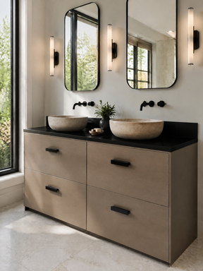 A modern double-sink bathroom vanity with a matte taupe cabinet, black countertop, and two vessel sinks, shown in a bright bathroom setting with mirrors, wall sconces, and a window.