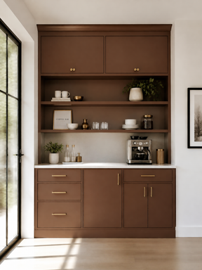 A tall built-in kitchen cabinet unit in warm medium brown wood, featuring upper and lower cabinets, open shelves, a white countertop, and brass-toned handles. The cabinet is styled with kitchenware, plants, and a coffee machine, set against a white wall with a window and framed art nearby.
