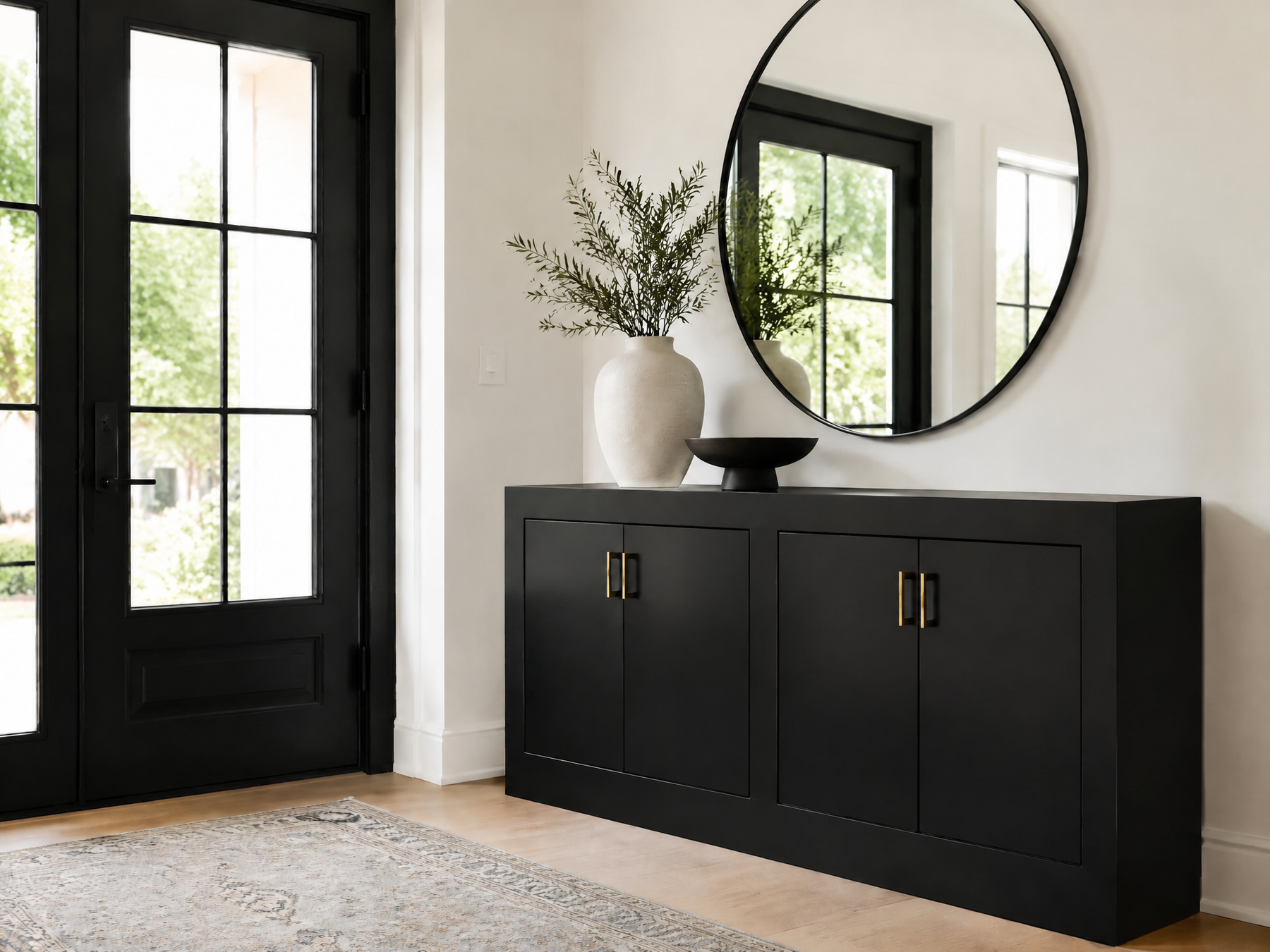 Modern entryway with a black cabinet, brass hardware, round mirror, and black-framed glass door.
