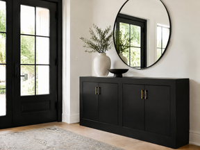 Modern entryway with a black cabinet, brass hardware, round mirror, and black-framed glass door.