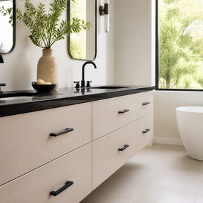 A modern bathroom vanity with a matte beige cabinet, a black countertop, and black hardware, shown in a bright room with a window, mirrors, and a white freestanding tub.