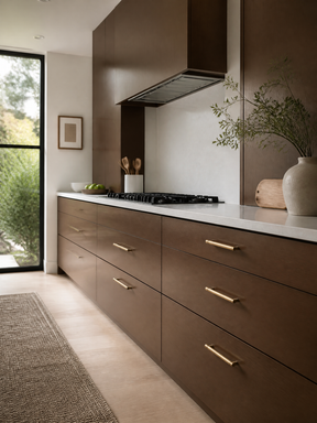 Modern kitchen with dark brown cabinets, brass handles, white countertops, and a black gas cooktop.