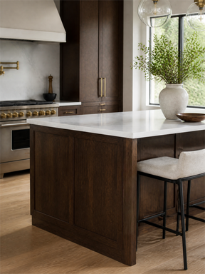 A modern kitchen island with dark wood cabinetry and a white stone countertop, styled with a large ceramic vase of greenery and two bar stools in a bright kitchen setting.