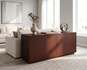 A modern wooden sideboard or credenza in a warm reddish-brown finish, styled in a bright living room next to a beige sofa with decorative vases and a metallic sculpture on top.