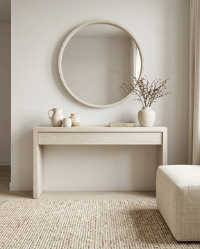 Minimalist entryway with a light wood console table, round mirror, ceramic vases, and textured neutral rug.